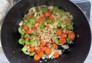 black cast iron pot with chopped celery, carrots, white onions, and minced garlic.