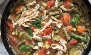 large pot of chicken minestrone soup with shredded chicken, celery, carrots, green beans, diced tomatoes, and spinach.