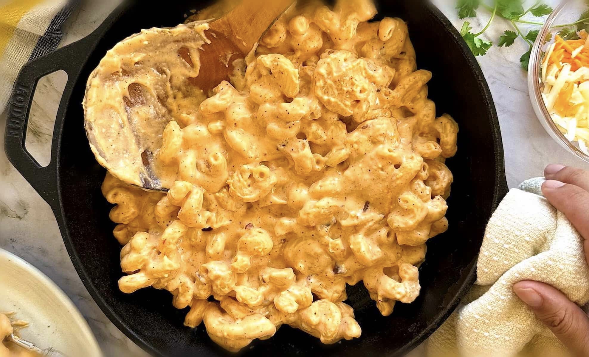 creamy chipotle mac and cheese in a cast iron skillet with a wooden spoon.