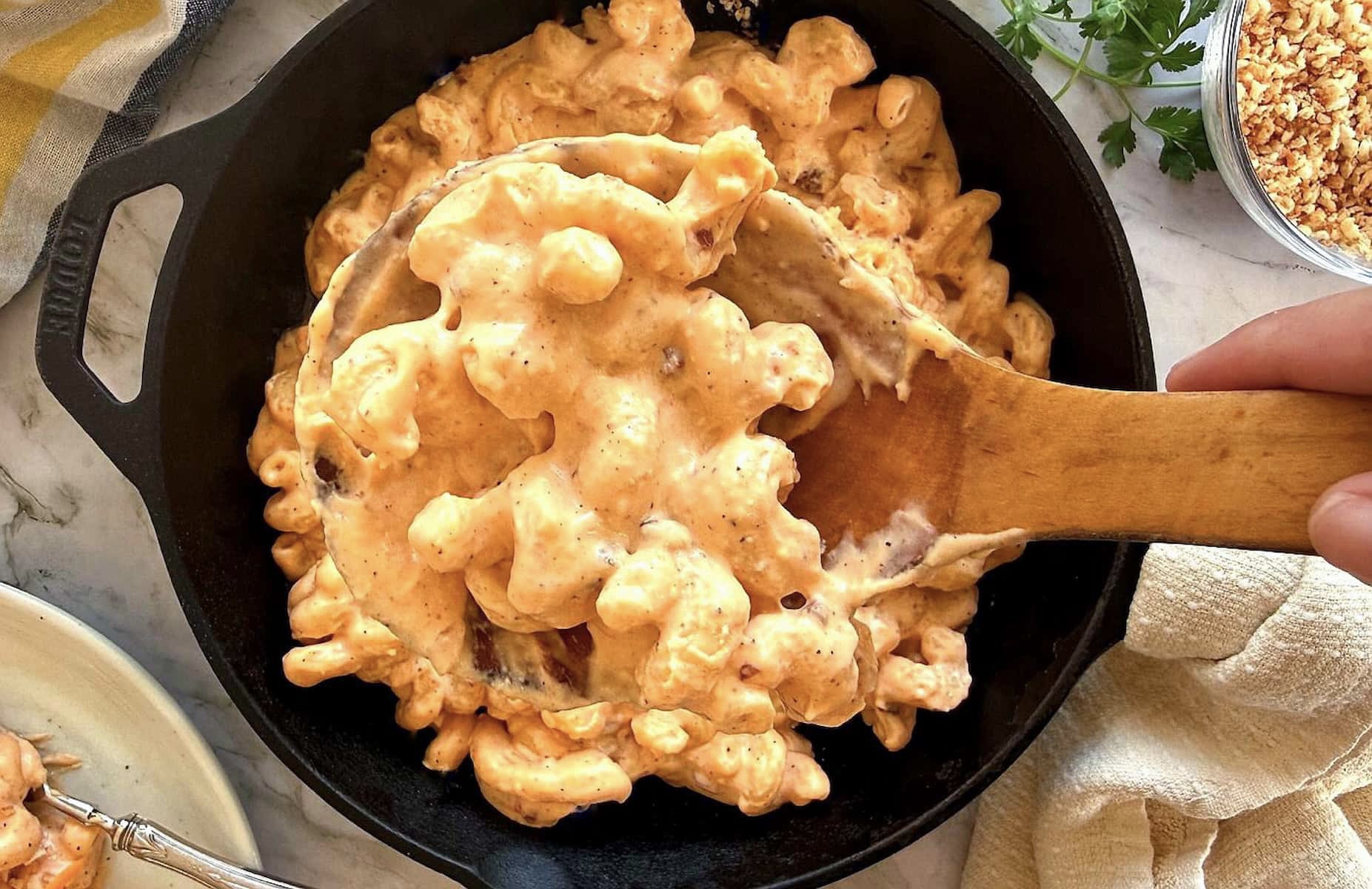 wooden spoon full of chipotle mac and cheese over a cast iron skillet with more.