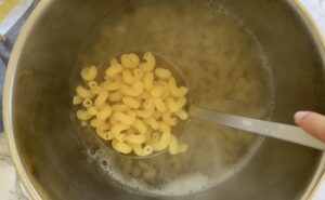 cavatappi pasta on a slotted spoon over a pot with more in water.
