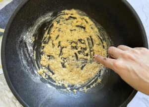 hand with a little whisk whisking an orange roux in a pan.