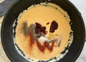 thick orange cheese sauce topped with chipotle peppers and spices in a black pan.