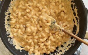 creamy mac and cheese in a black pan with a small rubber spatula.