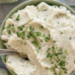 bowl of cottage cheese mashed potatoes topped with chives, two spoons in the bowl.