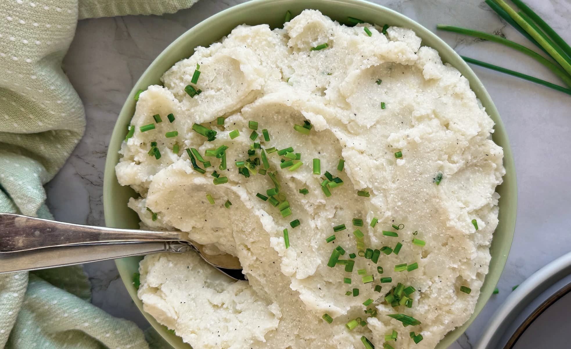 bowl of cottage cheese mashed potatoes topped with chives, two spoons in the bowl.
