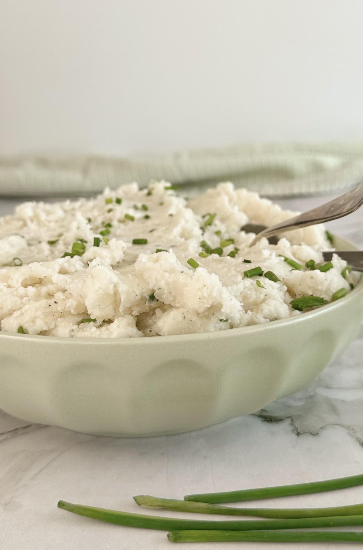 side view of cottage cheese mashed potatoes with chives in a green bowl with a spoon.