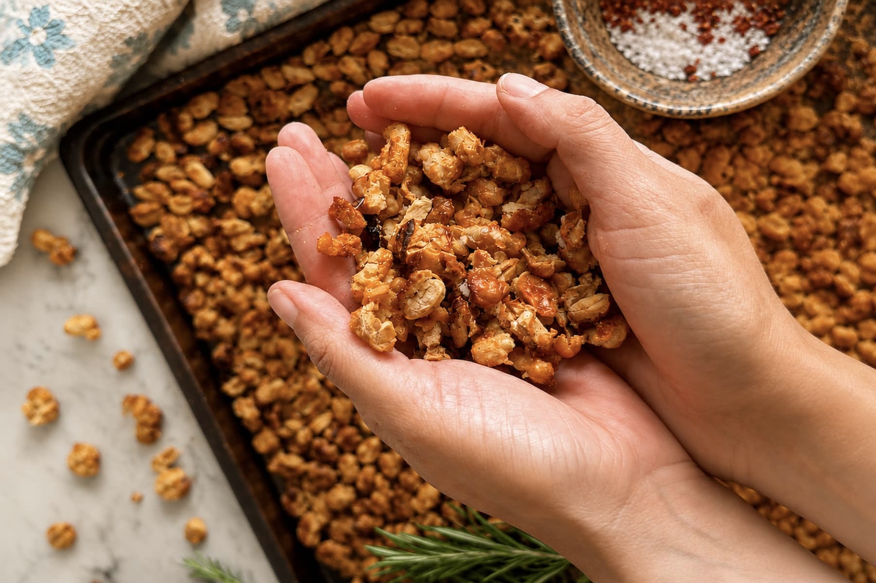crispy white beans in the palms of two hands over a sheet pan with more.