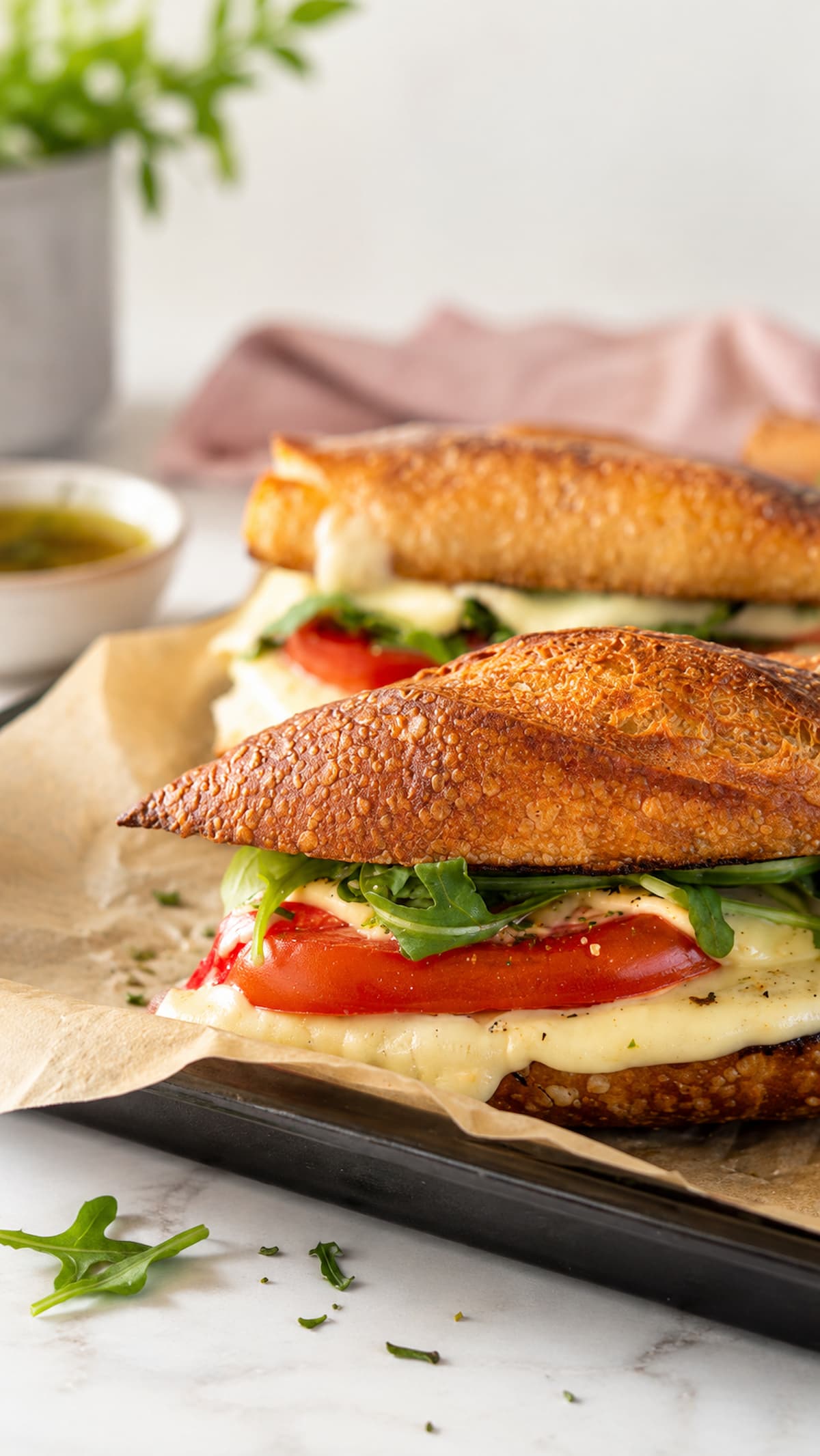 two caprese melt sandwiches on a parchment lined baking sheet with tomatoes, arugula, and melty mozzarella.