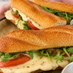 3 baguettes with arugula, tomatoes, and melty mozzarella on a parchment lined tray.
