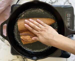 hand pressing an open faced baguette down in a cast iron skillet.