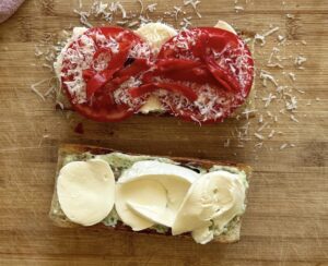 two slices of baguette - one side with green goddess sauce and sliced mozzarella cheese, the other side with sliced mozzarella cheese, tomatoes, roasted red peppers, and parmesan cheese.