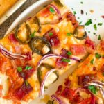 2 slices of maple bacon jalapeno pizza with red onions on a white plate next to a sheet pan with more.