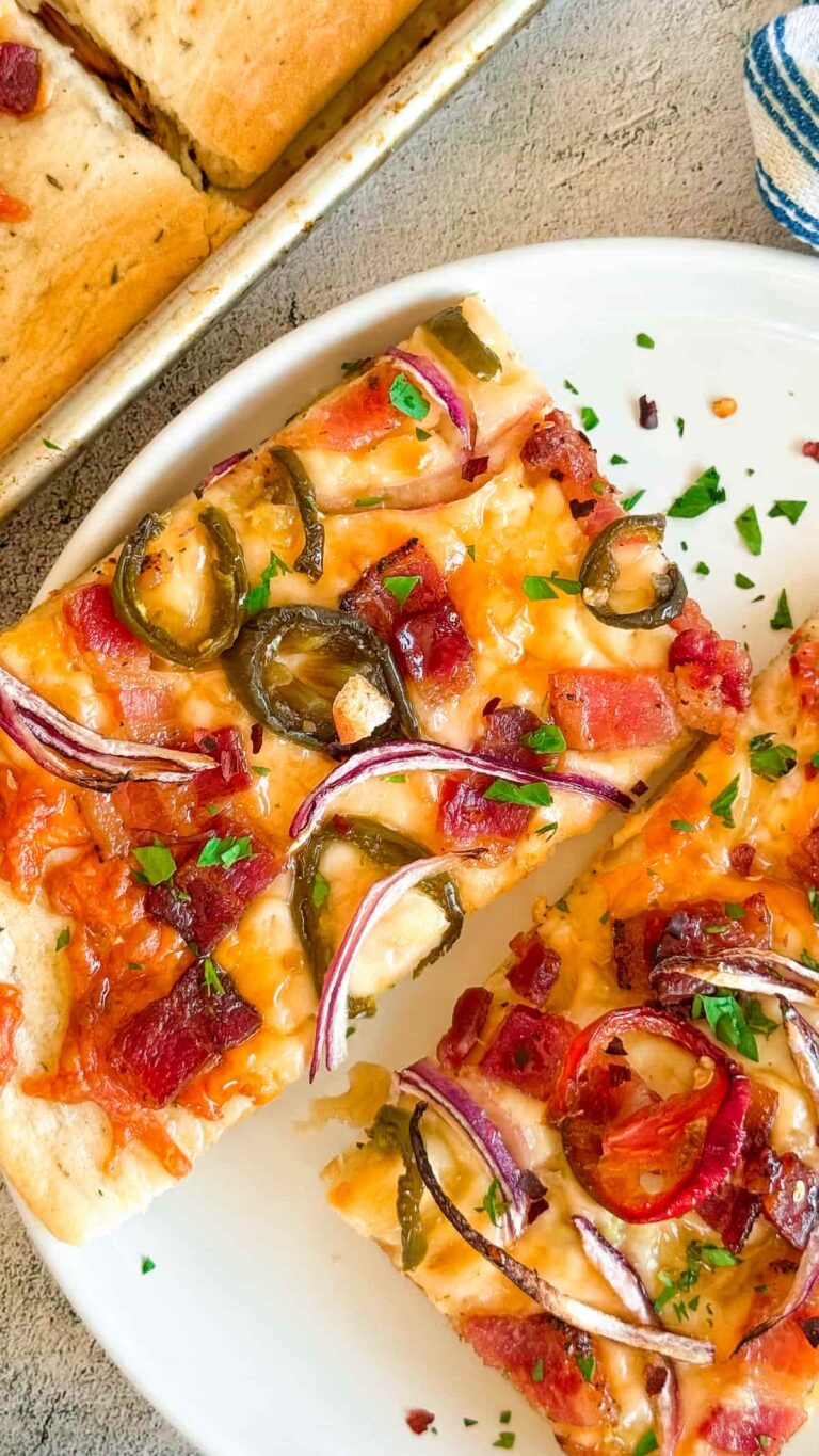 2 slices of maple bacon jalapeno pizza with red onions on a white plate next to a sheet pan with more.