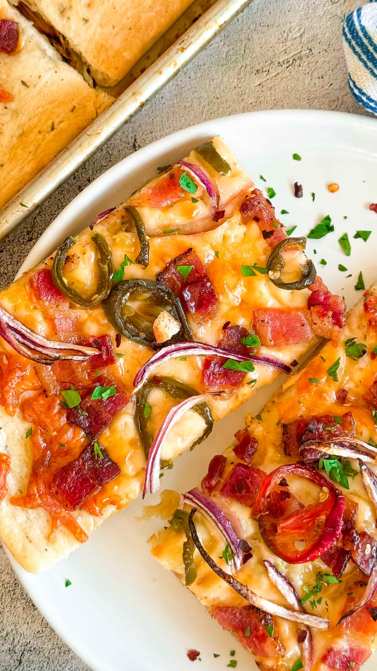 2 slices of maple bacon jalapeno pizza with red onions on a white plate next to a sheet pan with more.
