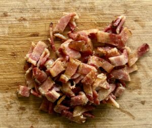 pile of pieces of bacon coated in maple syrup on a cutting board.