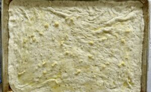 raw pizza dough on a sheet pan topped with minced garlic and olive oil.