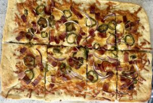 cooked pizza topped with bacon, sliced jalapenos, and red onions.