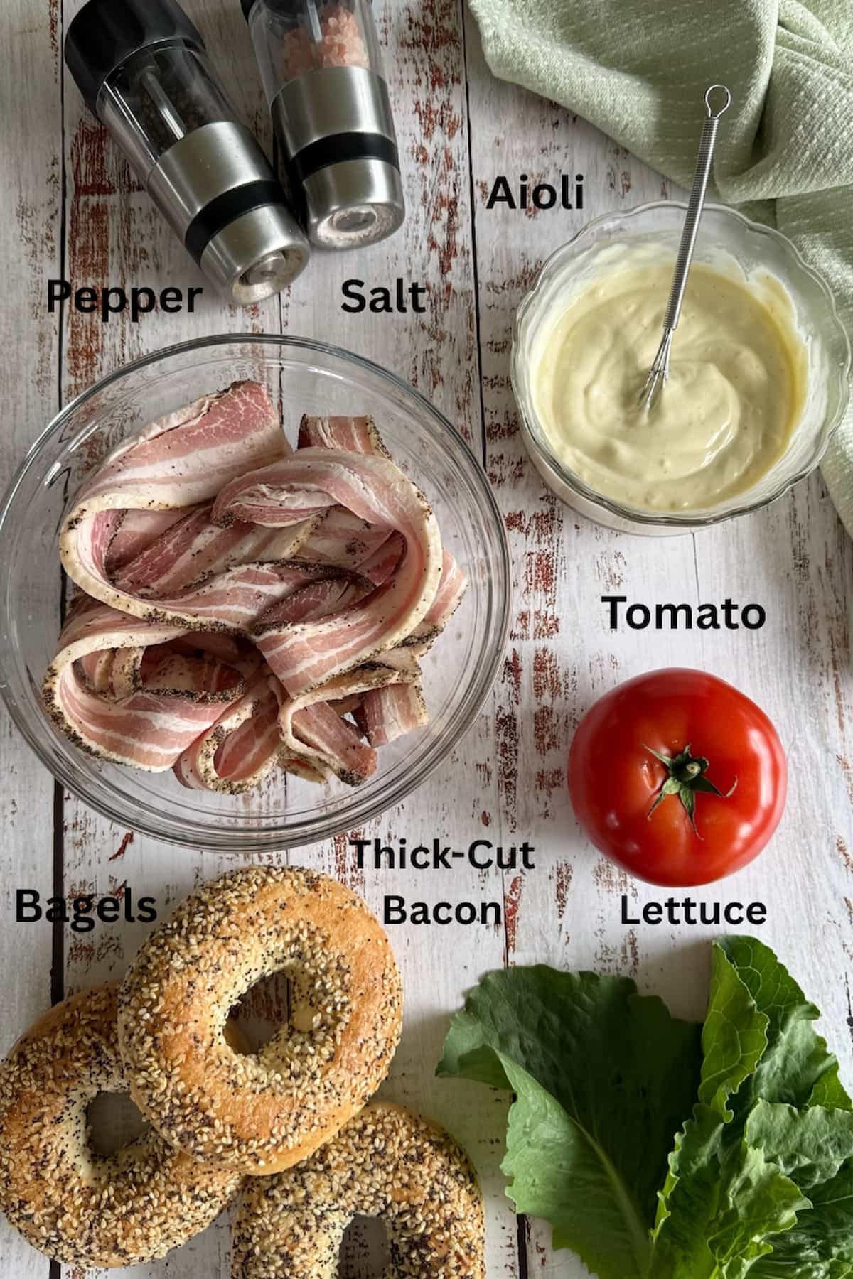 ingredients for bagel BLTs laid out - thick-cut bacon, tomato, aioli, salt, pepper, lettuce, and everything bagels.