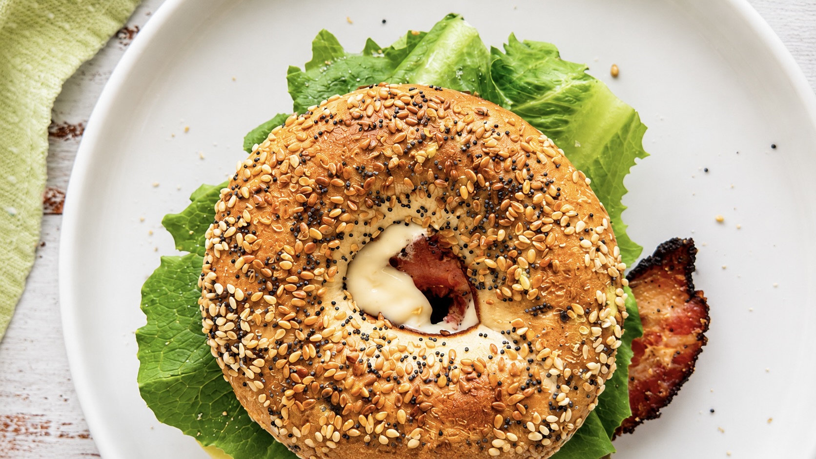 Top view of a BLT bagel with crispy bacon, lettuce, and creamy mayo on an everything bagel.