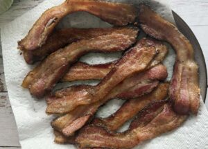 cooked crispy thick cut bacon pieces on a paper towel lined plate.