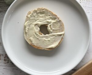 1 slice of a bagel topped with garlic mayo on a white plate.