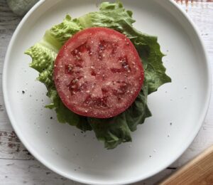sliced of tomato with salt and pepper on a piece of lettuce on a white plate.