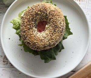 everything bagel on a plate with lettuce, tomatoes, bacon, and aioli.