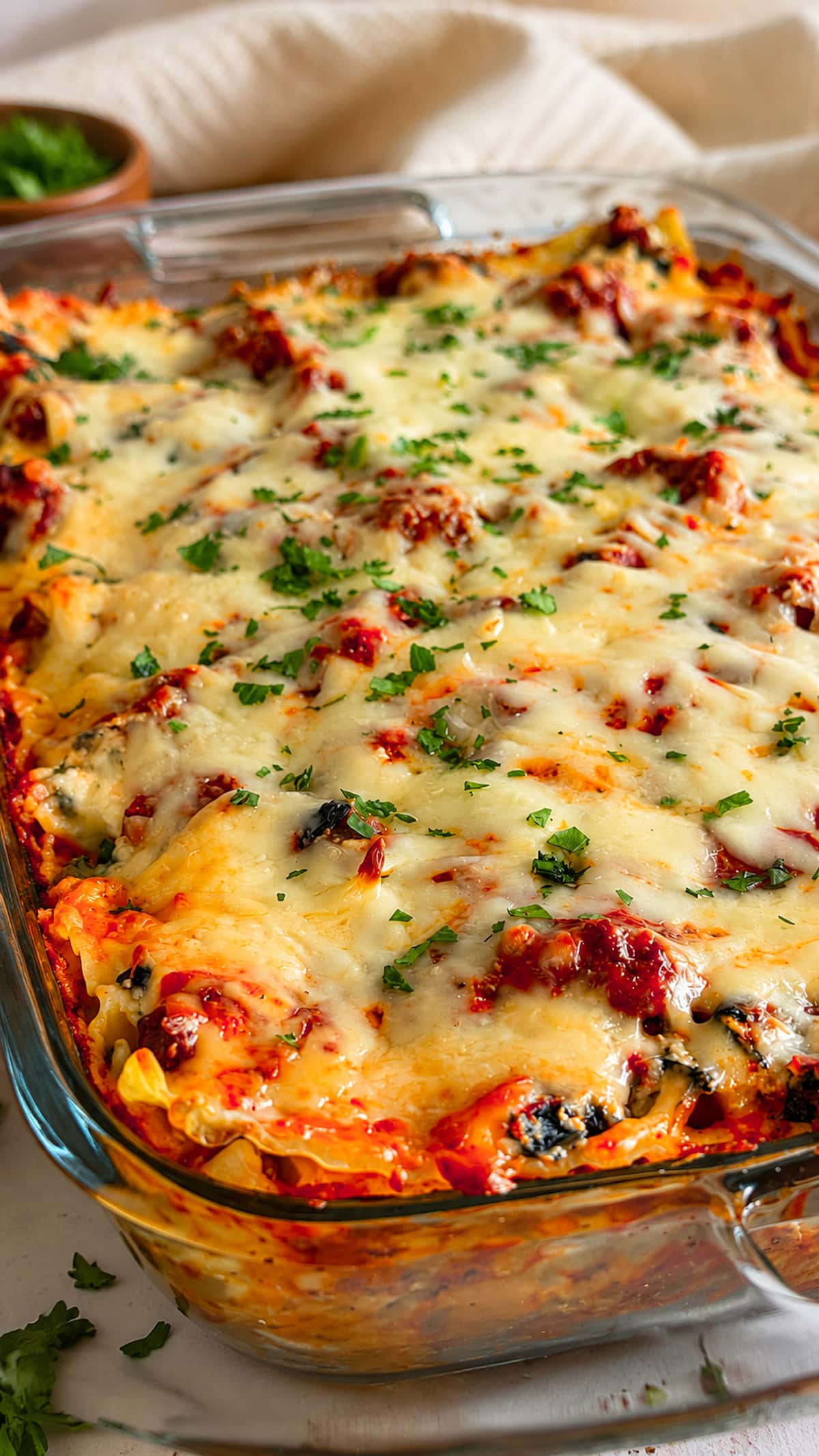 Spinach and Ground Beef Lasagna baked in a glass casserole dish with layers of pasta, seasoned beef, spinach, and melted cheese, garnished with fresh parsley.