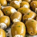 Close up of green olives stuffed with creamy blue cheese garnished with fresh chopped parsley arranged on a white plate.