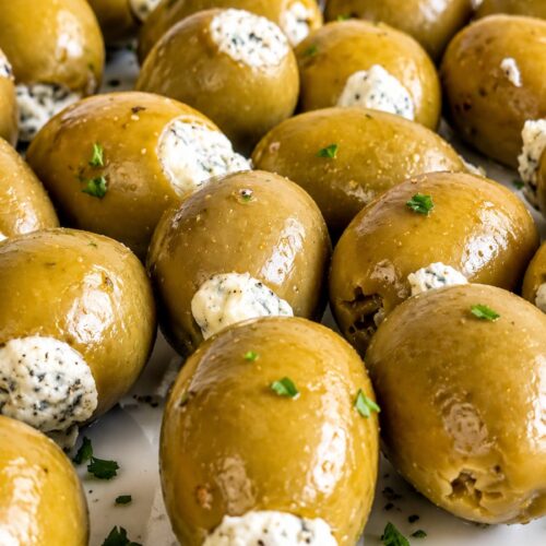 Close up of green olives stuffed with creamy blue cheese garnished with fresh chopped parsley arranged on a white plate.
