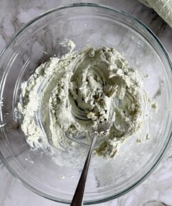 cream cheese mixture with blue cheese crumbles in a glass bowl with a spoon.