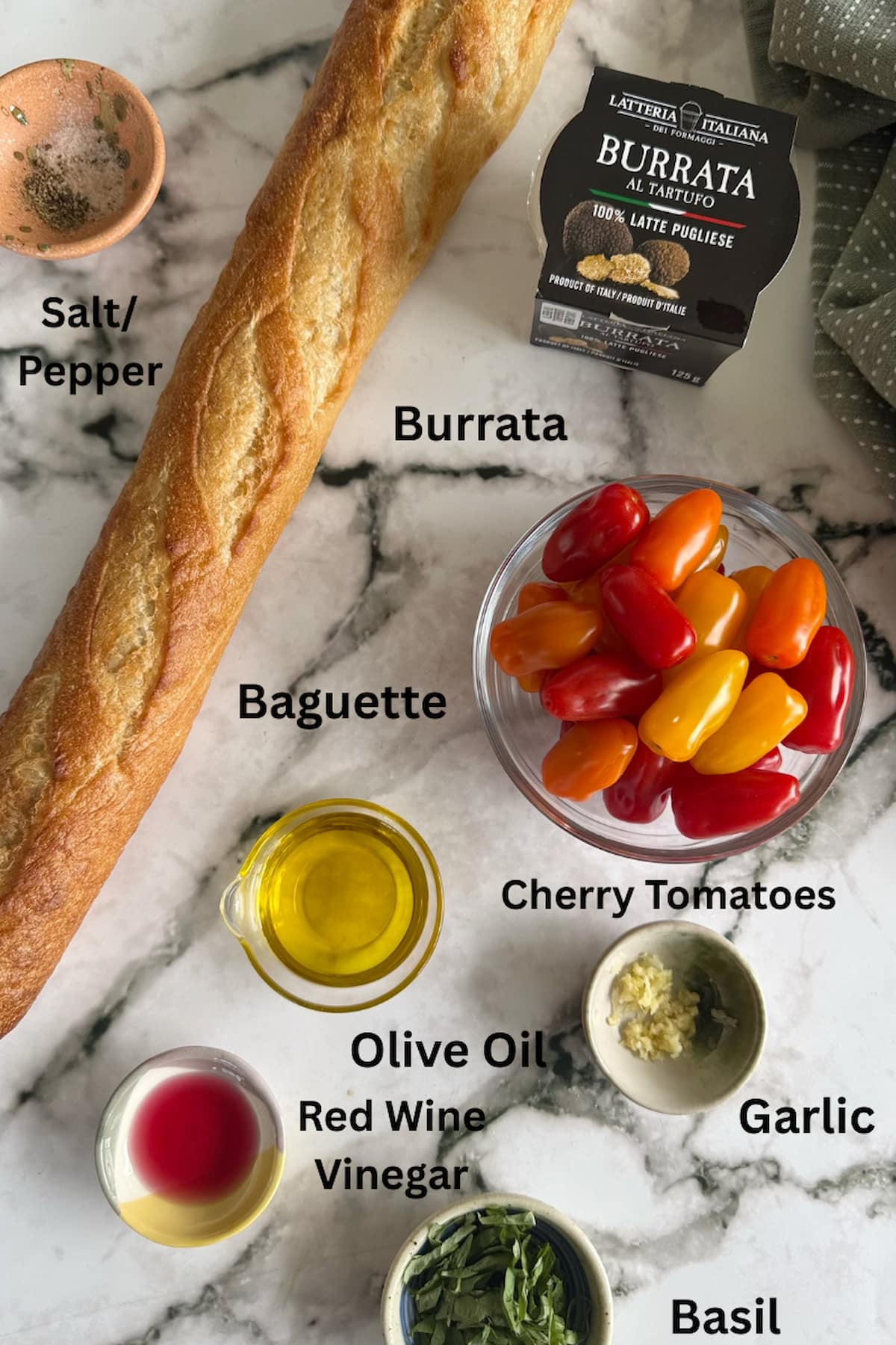 ingredients for burrata bruschetta laid out in separate bowls next to a fresh baguette - salt/pepper, burrata cheese, cherry tomatoes, olive oil, red wine vinegar, basil, and garlic.