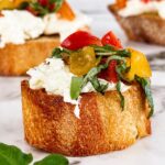 Burrata bruschetta made with creamy burrata cheese, marinated cherry tomatoes, and fresh basil on toasted artisan bread, photographed on a marble surface with a soft, blurred background.