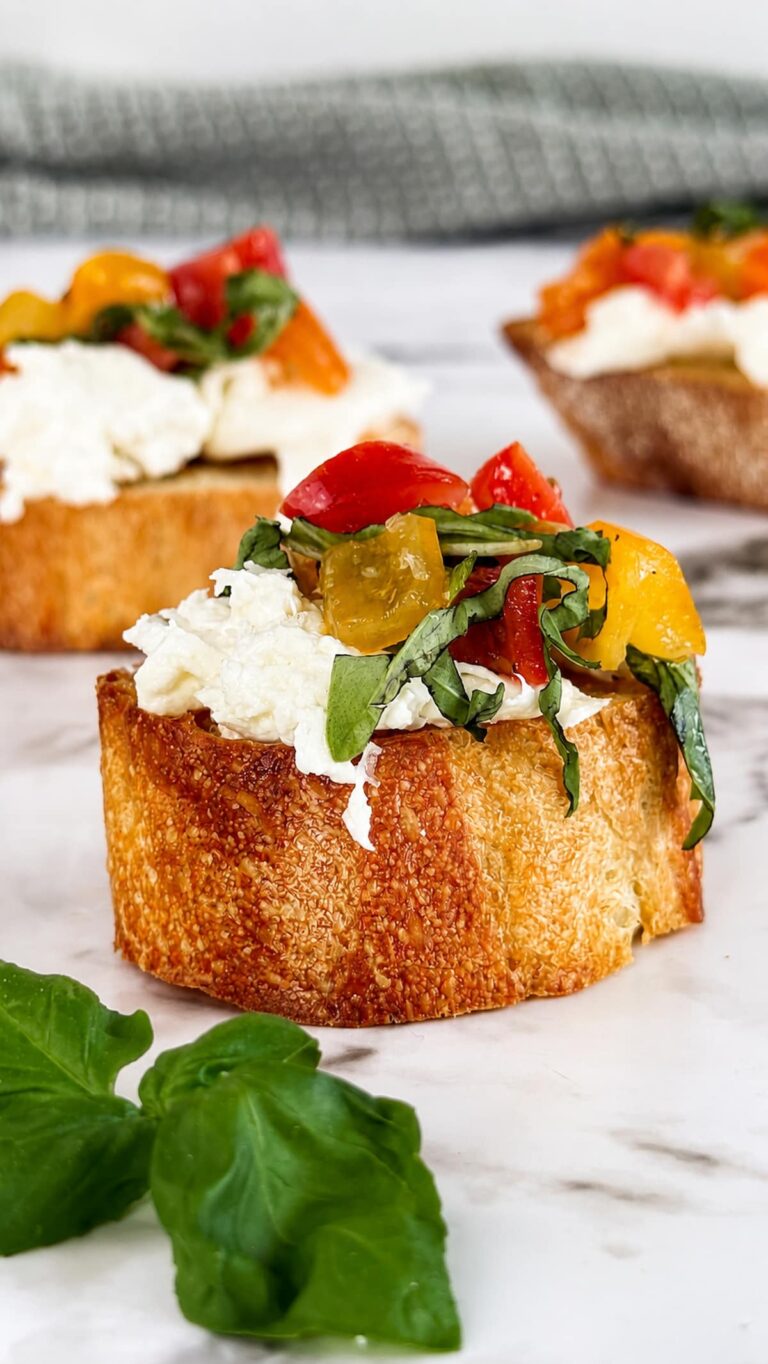 Burrata bruschetta made with creamy burrata cheese, marinated cherry tomatoes, and fresh basil on toasted artisan bread, photographed on a marble surface with a soft, blurred background.