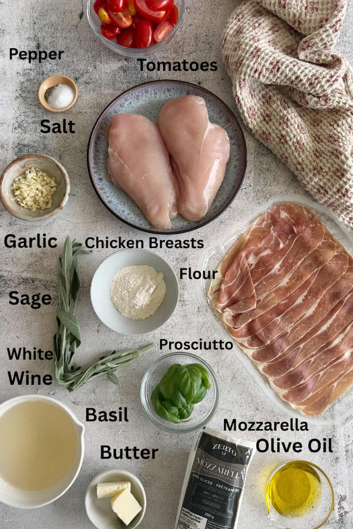 ingredients for caprese chicken saltimbocca laid out in separate bowls - tomatoes, salt, pepper, chicken breasts, sage, basil, white wine, olive oil, mozzarella, prosciutto, flour, butter, and garlic.