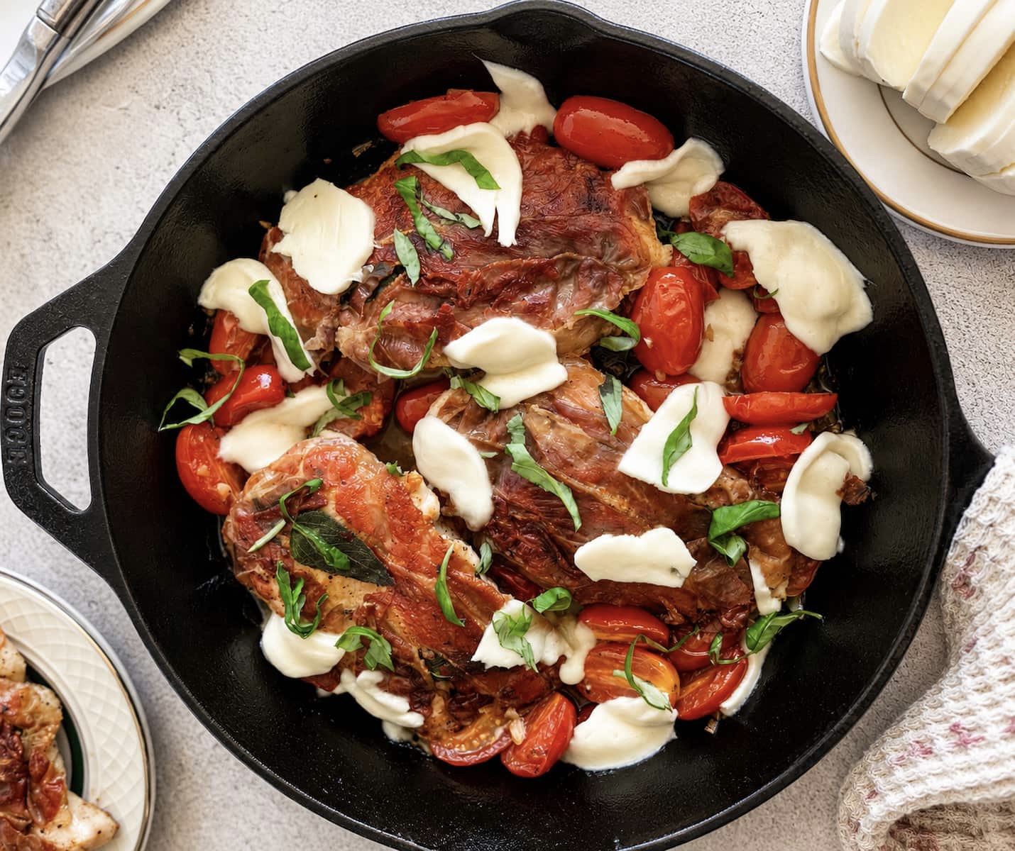 Caprese chicken saltimbocca in a cast iron skillet with prosciutto wrapped chicken, fresh mozzarella, roasted cherry tomatoes, and basil.