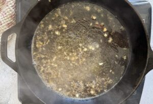 minced garlic cooking in white wine in a cast iron skillet.