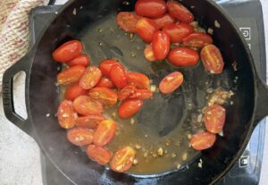 halved cherry tomatoes and minced garlic cooking in wine in a cast iron skillet on an induction cook top.