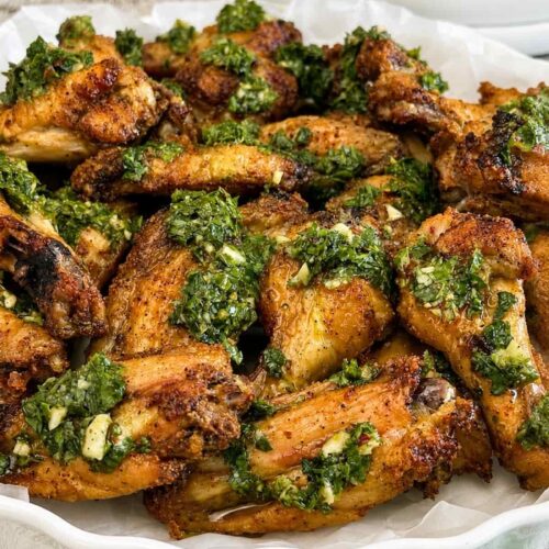 Close up of crispy baked chimichurri chicken wings topped with garlic herb sauce and served with extra chimichurri on the side.