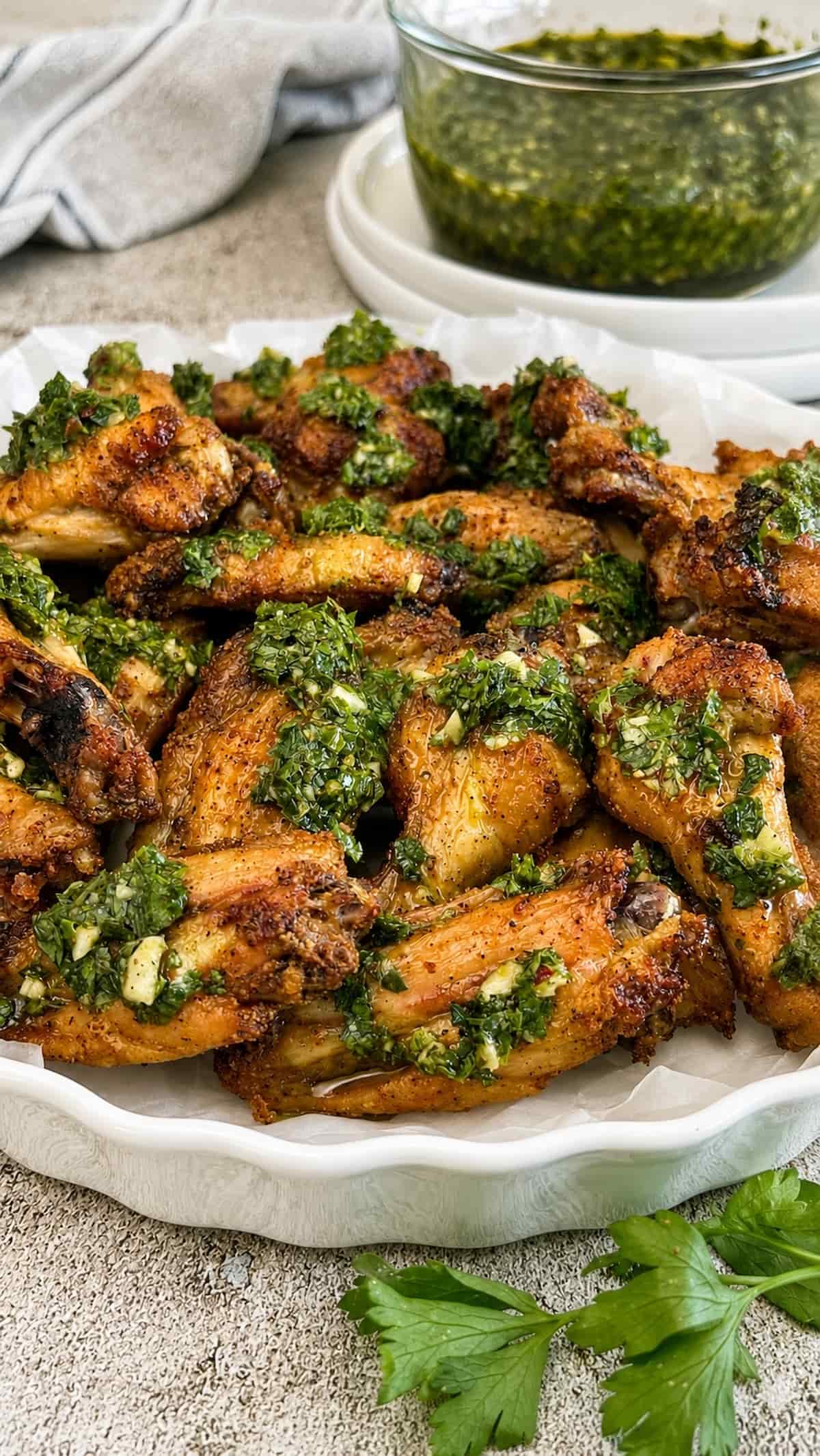 Close up of crispy baked chimichurri chicken wings topped with garlic herb sauce and served with extra chimichurri on the side.