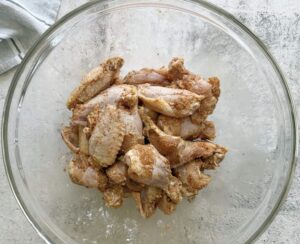 raw seasoned chicken wings in a large glass bowl.