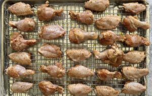 raw seasoned chicken wings laid out in a single layer on a wire rack foil lined baking sheet.