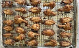 cooked crispy chicken wings laid out in a single layer on a wire rack foil lined baking sheet.