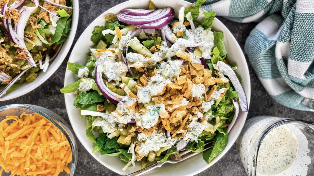 Chopped dill pickle salad topped with dill pickle ranch dressing, shredded cheese, red onion, chopped pickles, and crispy onions.