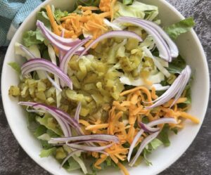 Chopped dill pickle salad with romaine lettuce, green cabbage, cheddar cheese, red onion, and dill pickles in a white bowl.