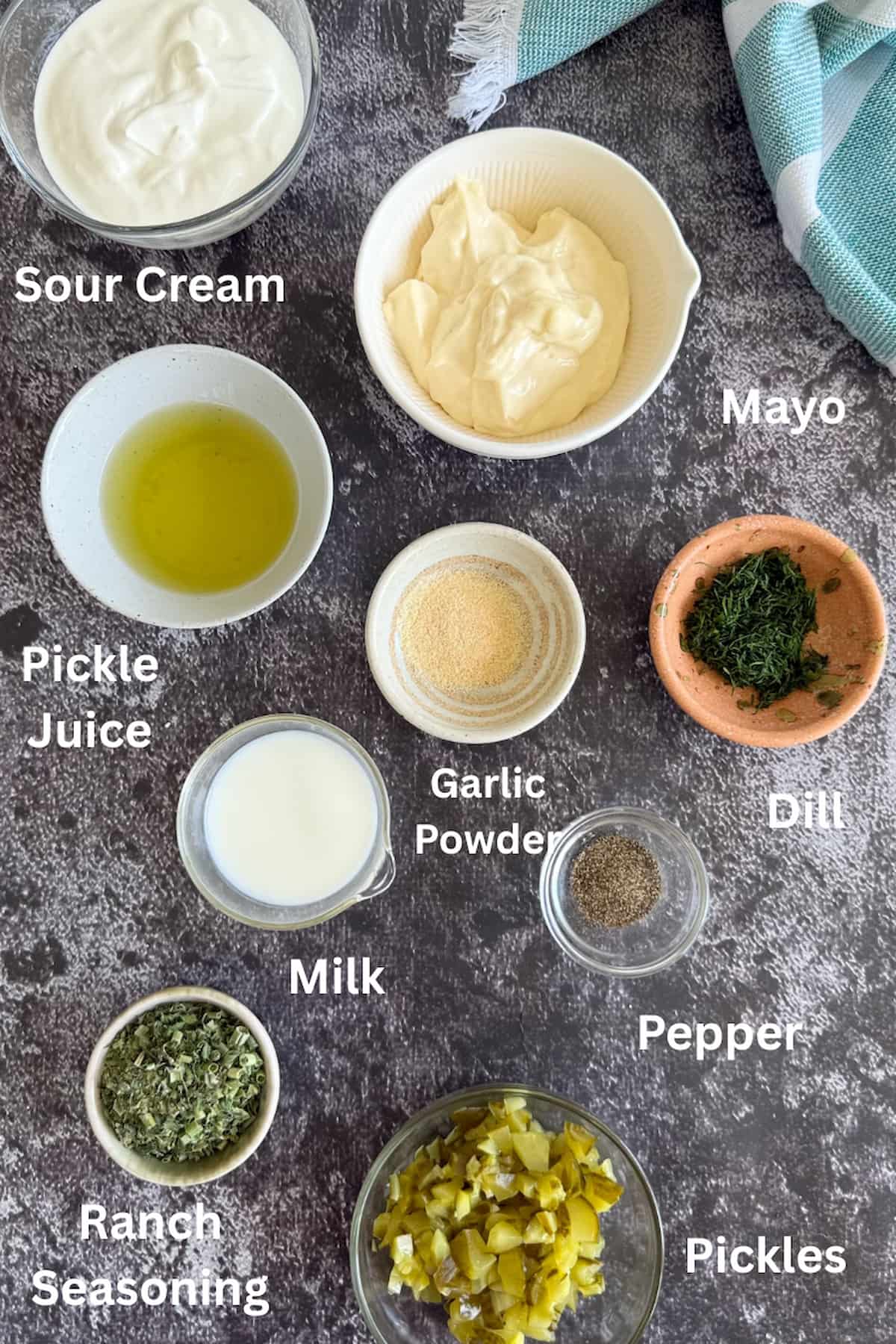 ingredients for dill pickle ranch dressing laid out in separate bowls - sour cream, mayo, pickle juice, pepper, garlic powder, milk, ranch seasoning, dill, and pickles.