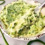 Spoonful of homemade garlic scape butter with fresh chopped garlic scapes in a rustic bowl.