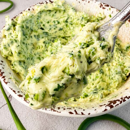 Spoonful of homemade garlic scape butter with fresh chopped garlic scapes in a rustic bowl.
