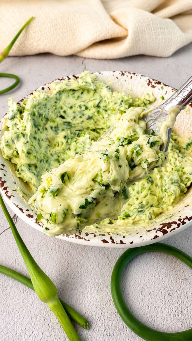 Spoonful of homemade garlic scape butter with fresh chopped garlic scapes in a rustic bowl.